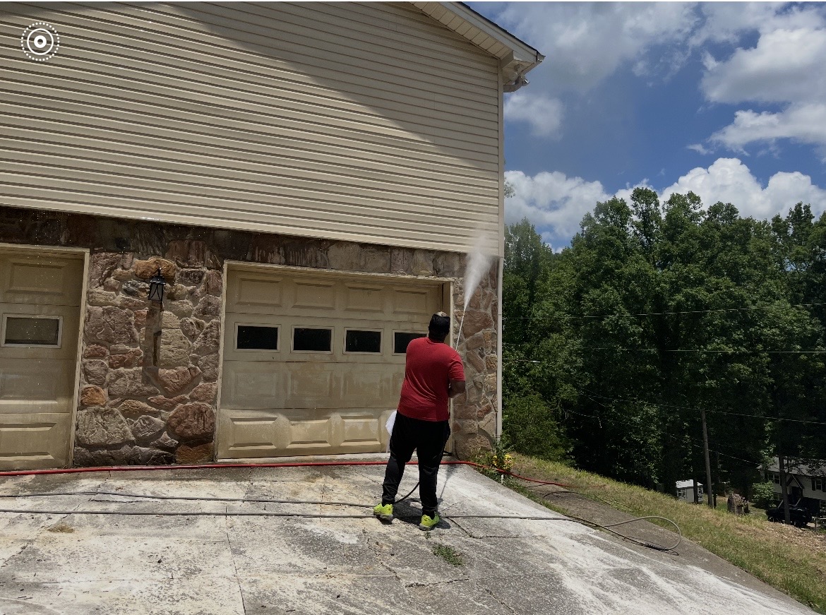Team member pressure washing the siding above a garage